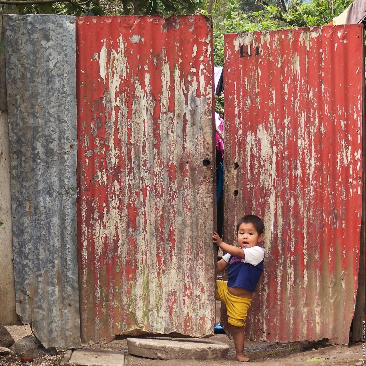 Boy opening a red lamina doorway around Antigua Guatemala by Rudy Giron